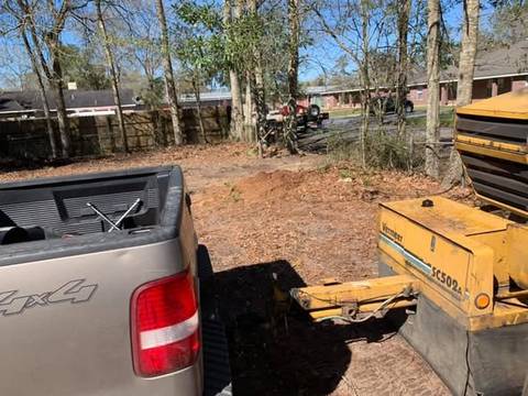 Pickup truck towing a stump grinder across a yard