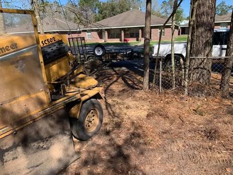 Yellow stump grinder in a back yard by a fence